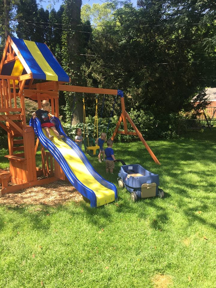 Child on a slide with other children playing on a swing set in a yard