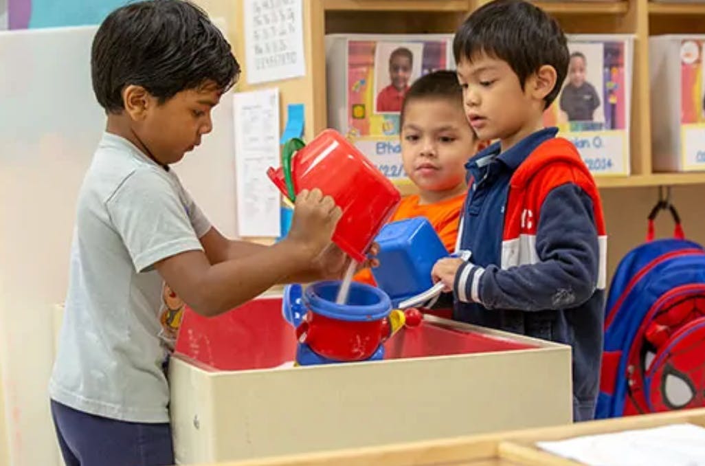 Three children playing with water and toys in a classroom