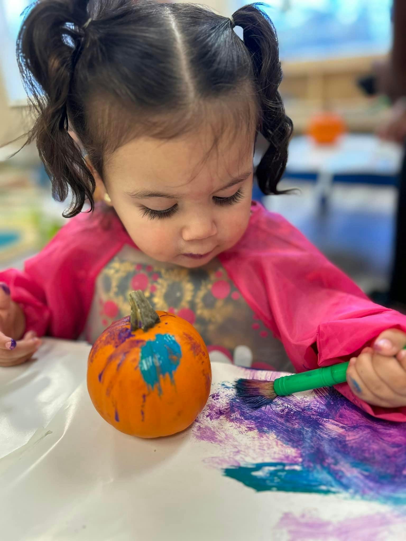 Child painting a small pumpkin with a paintbrush