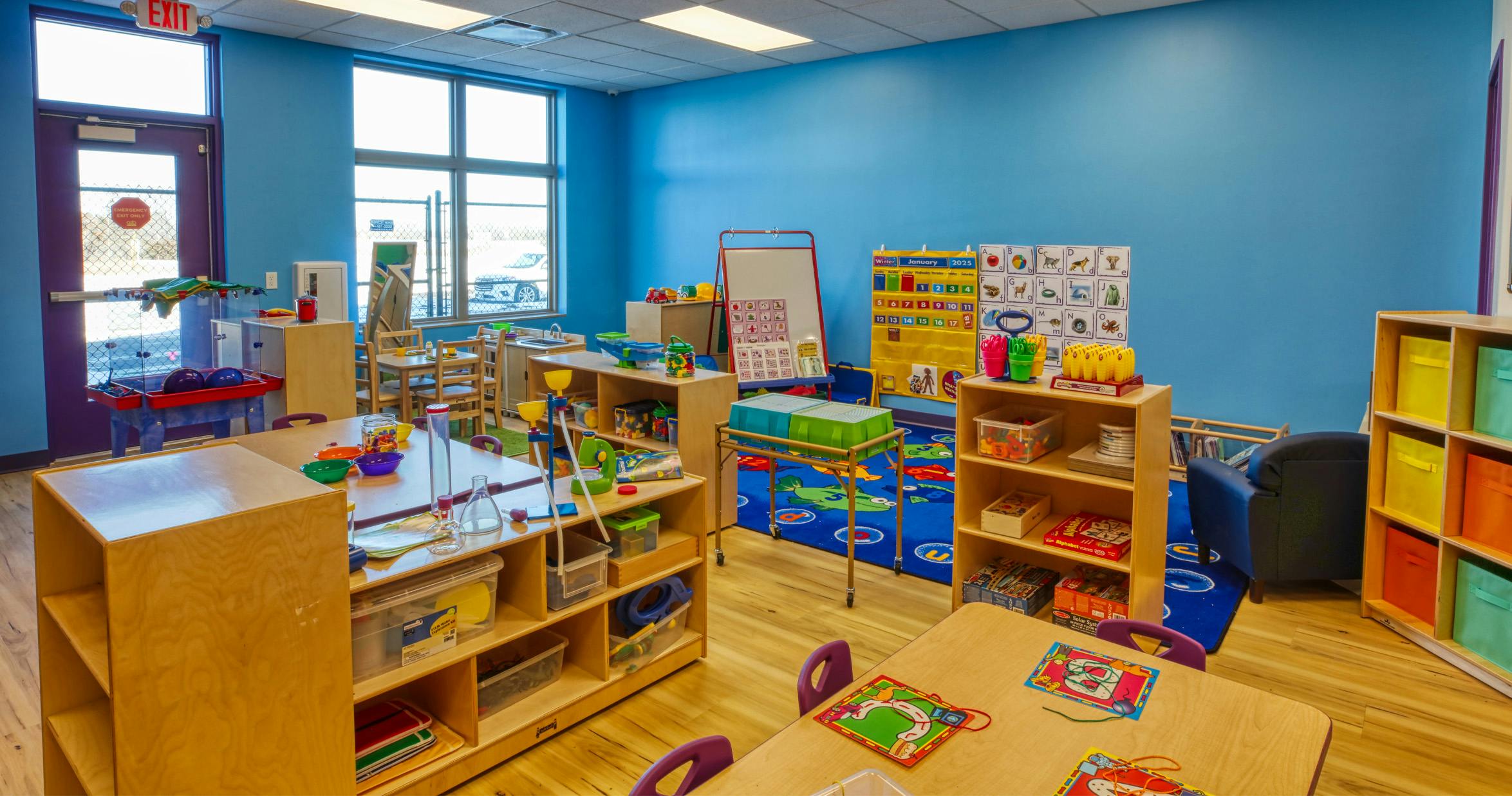 Classroom with small tables, chairs, bookshelves, and various learning materials