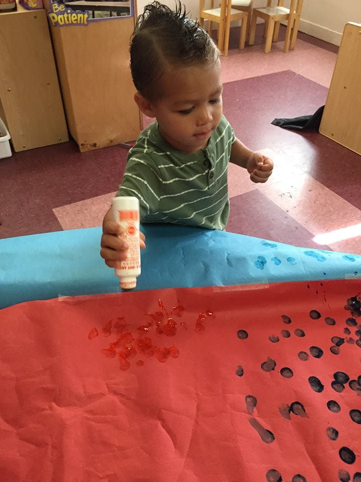 Child squeezing a bottle of red paint onto red paper