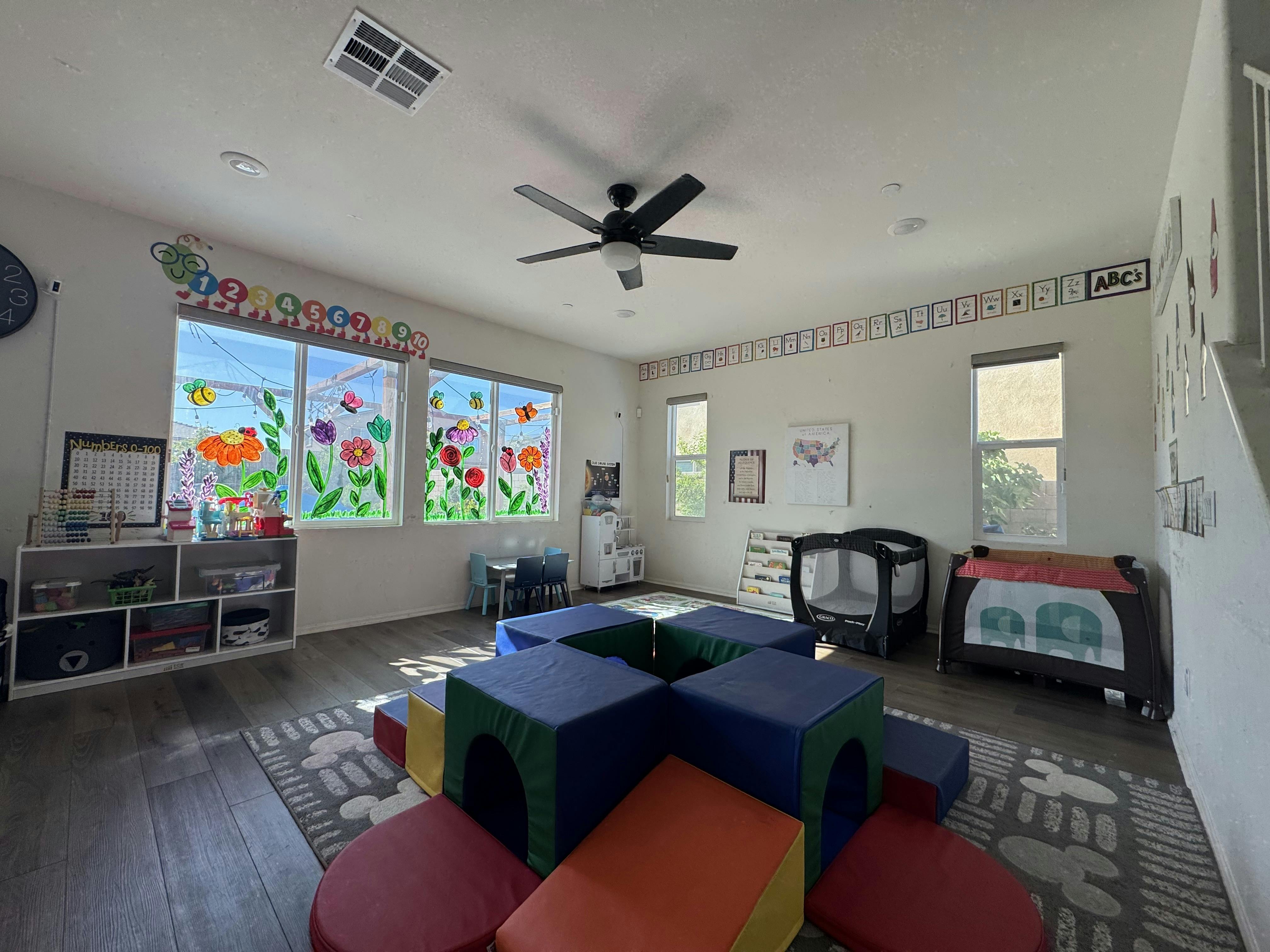 Childcare room with colorful play blocks, cribs, child-sized tables, and learning posters