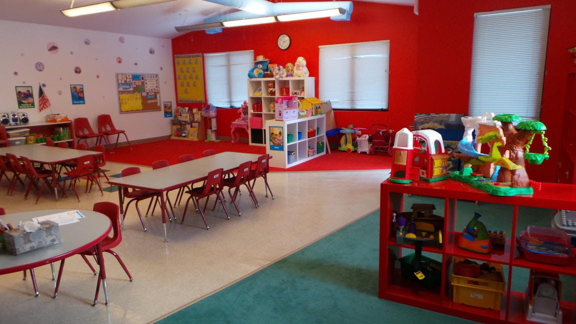 Classroom with small tables and chairs, shelves with toys
