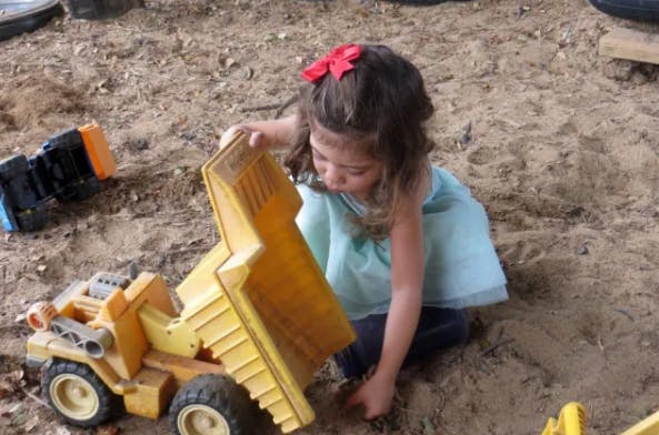 Child playing with a toy dump truck in sand