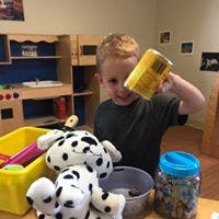 Child holding a yellow cup over a stuffed animal in a play kitchen