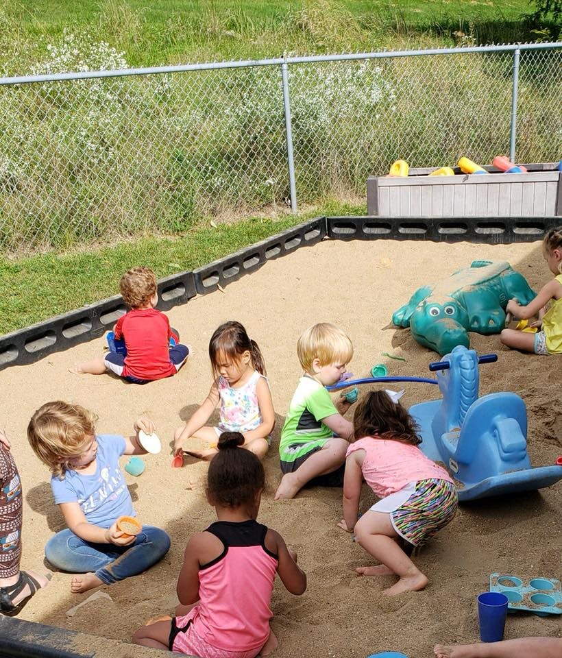 Multiple children playing in a sandbox with toys