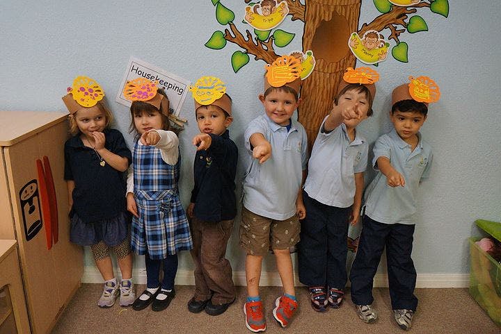 Six children wearing paper hats pointing forward in a classroom