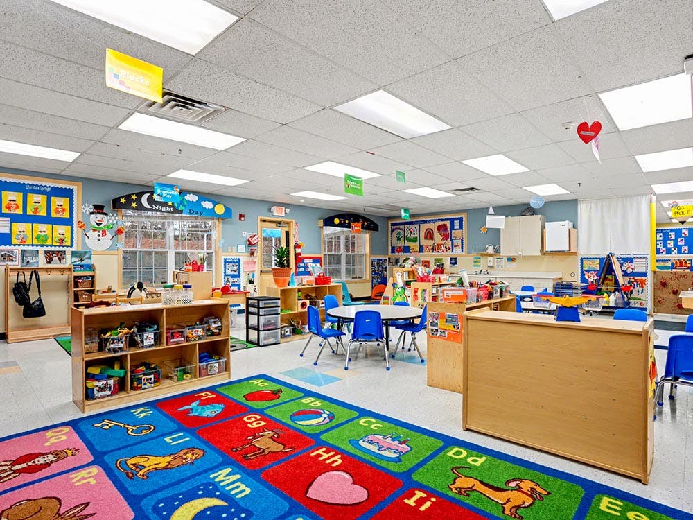 Colorful preschool classroom with an alphabet rug, small tables, and toy shelves