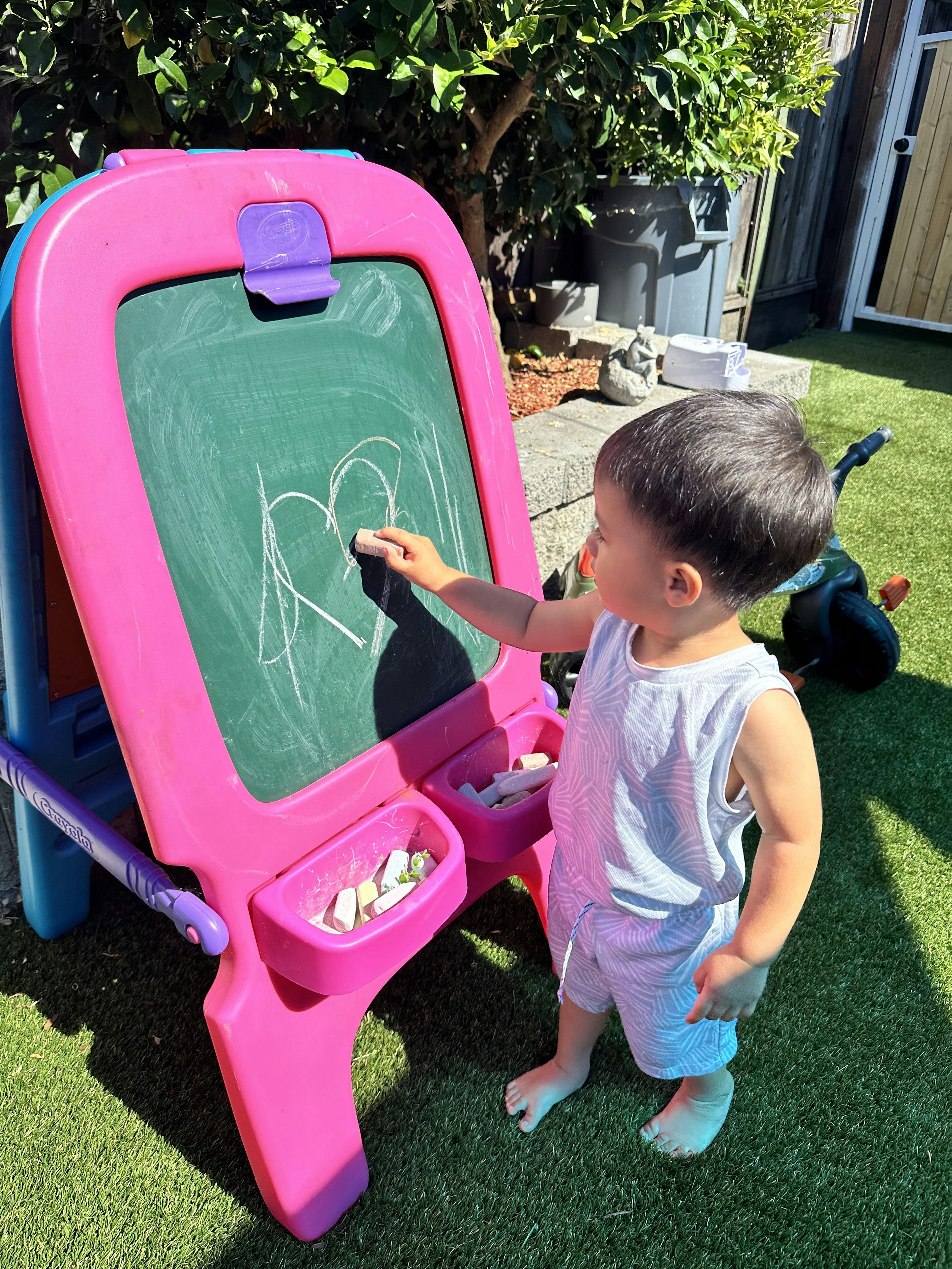 Child drawing a heart on a chalkboard easel outdoors
