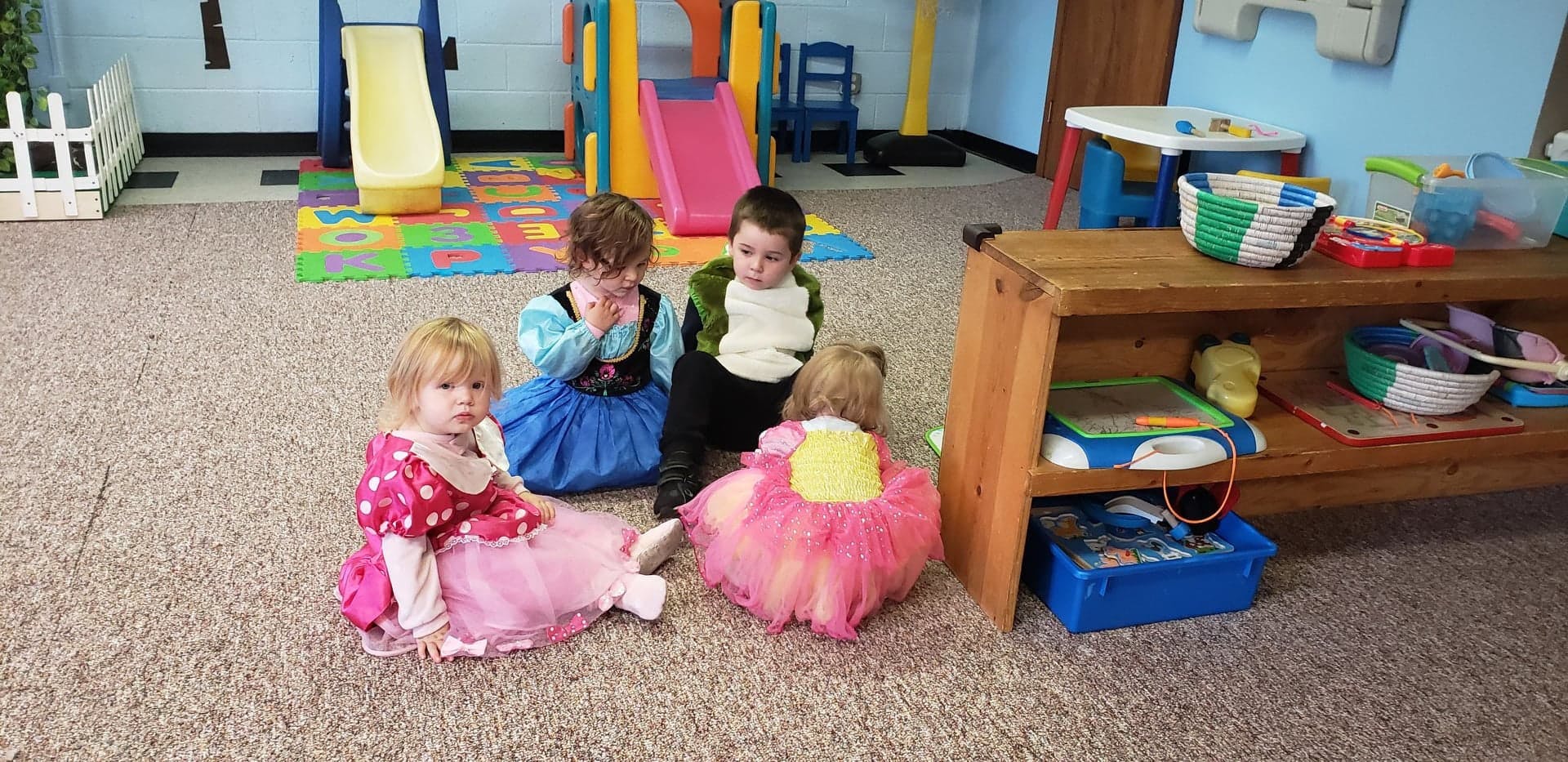 Four children sitting on a carpeted floor in a play area