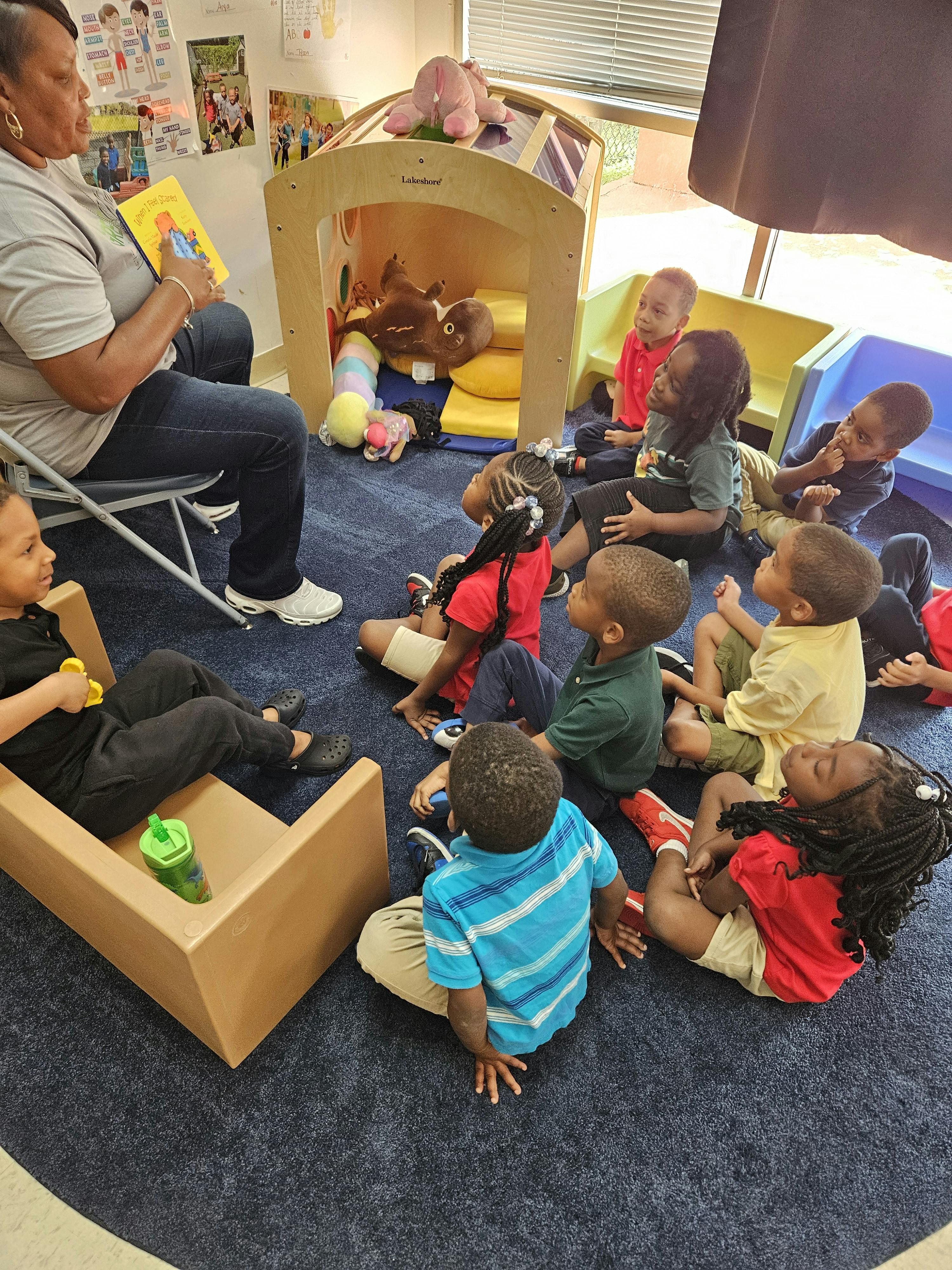 Person reading a book to a group of children in a classroom