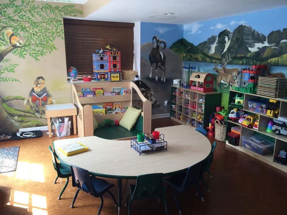 Classroom with murals, small tables, chairs, and shelves with toys and books