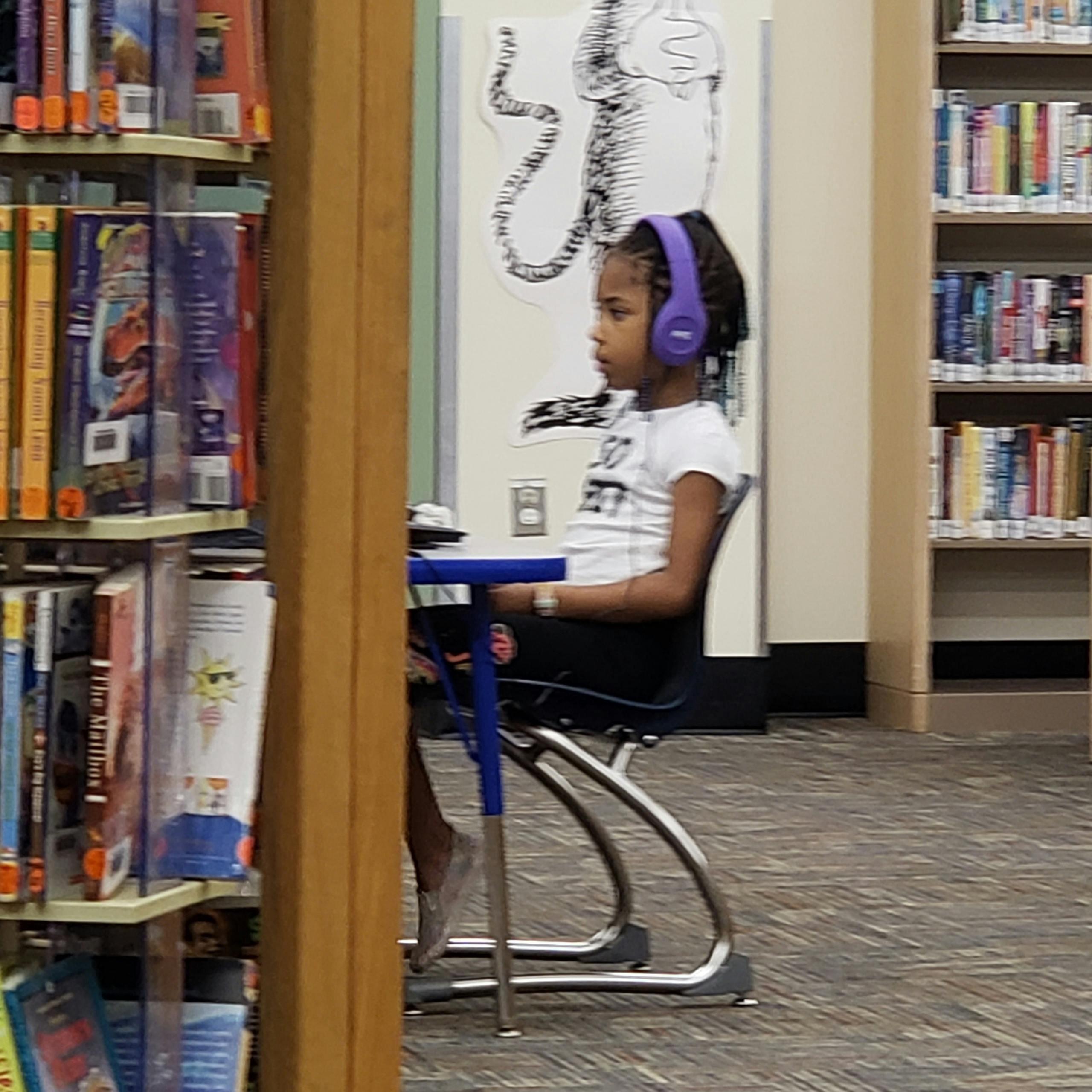 Child wearing headphones sitting at a desk in a library