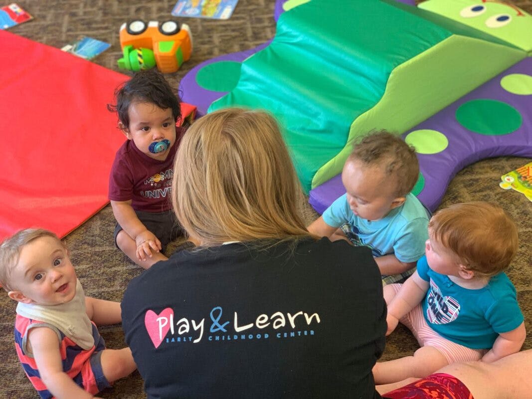Adult with four children sitting on the floor in a play area