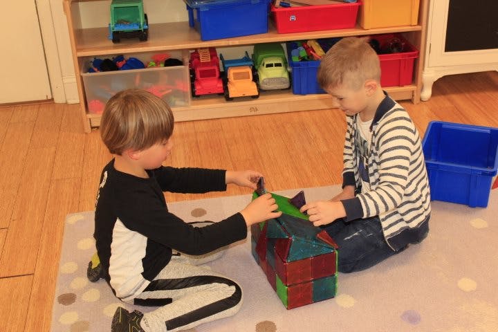 Two children playing with magnetic blocks on a rug