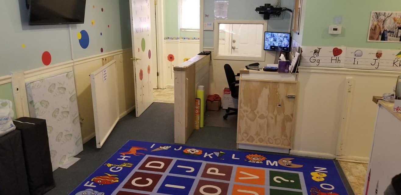Room with alphabet rug, cribs, and desk with a desk and computer monitor