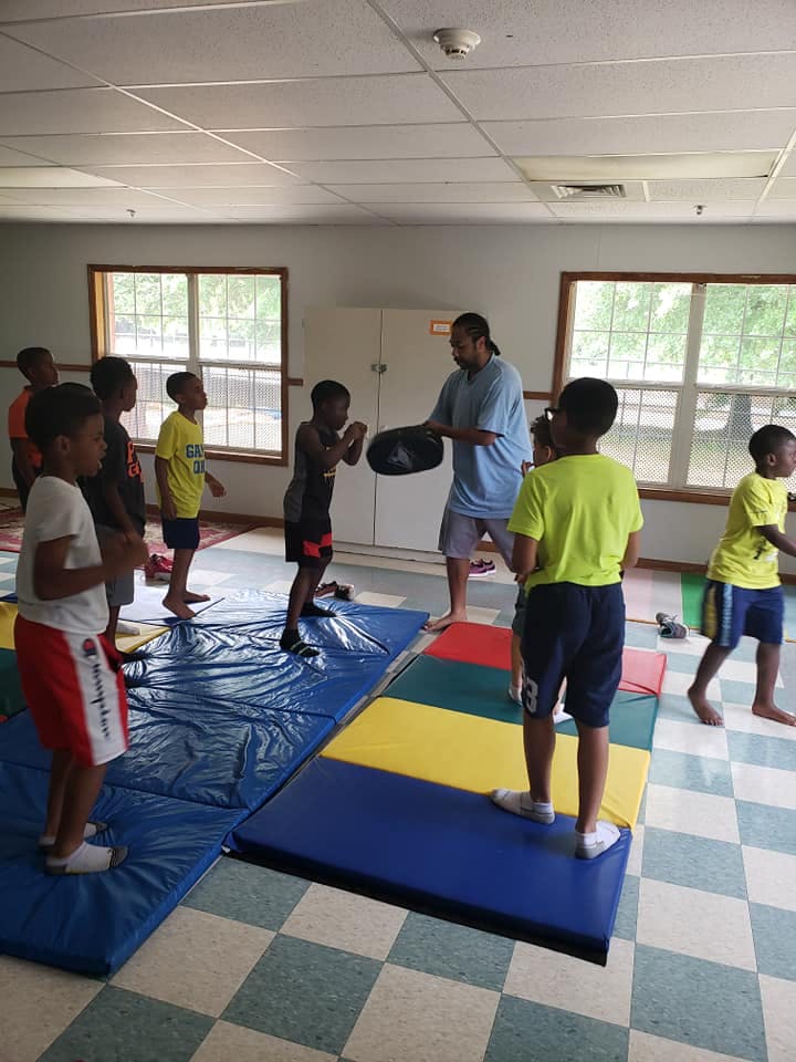 Adult holding a pad for a child to punch, other children watching