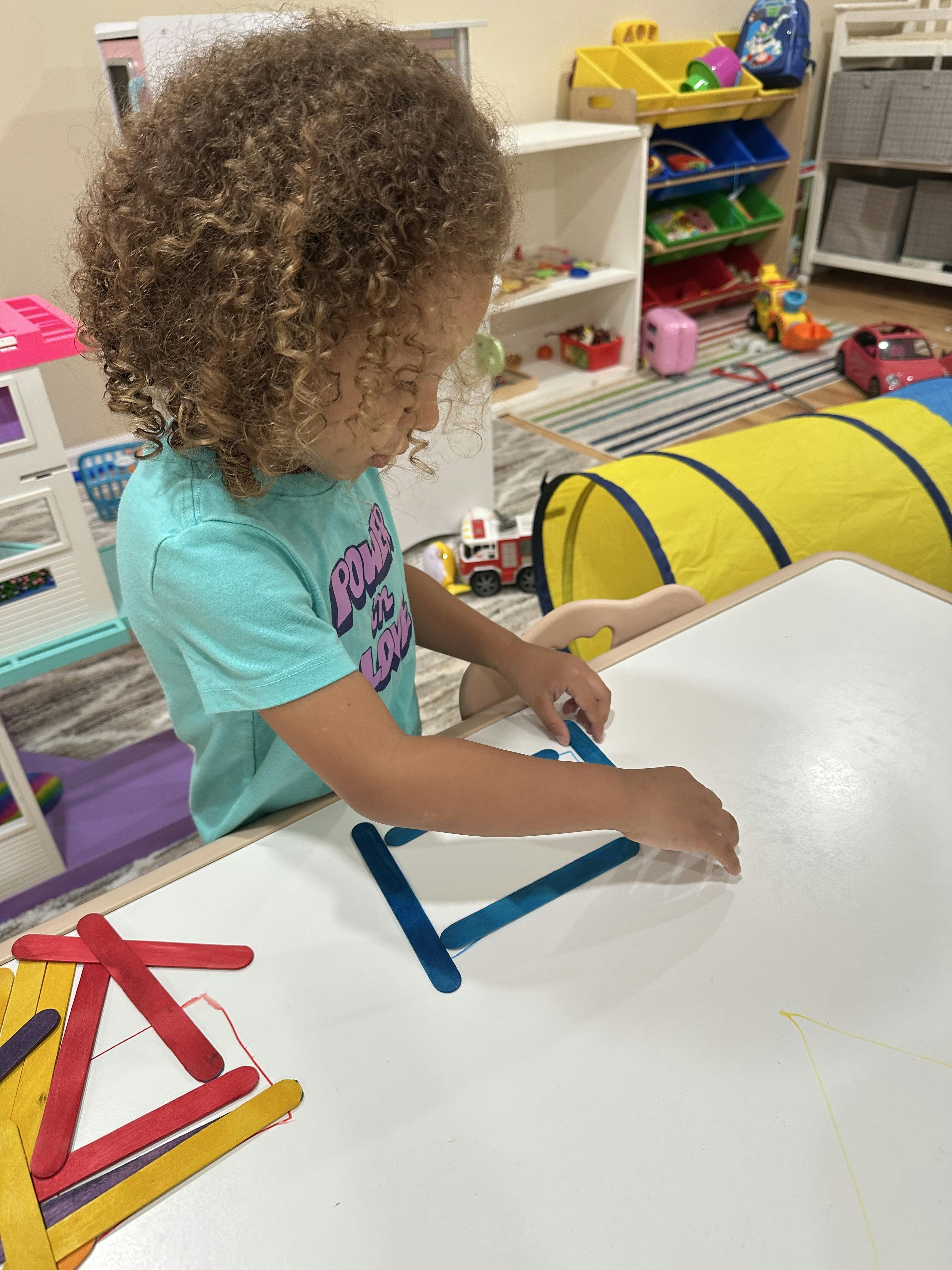 Child playing with craft sticks on a white table
