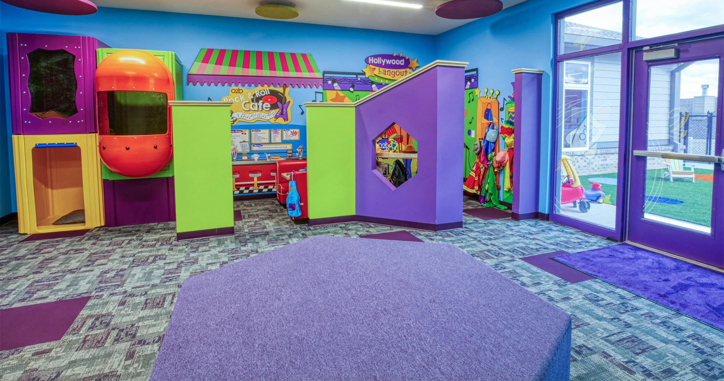 Colorful indoor play area with different sections and an outdoor play area visible through a glass door