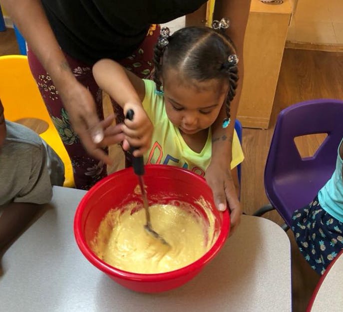 Person helping a child stir batter in a red bowl