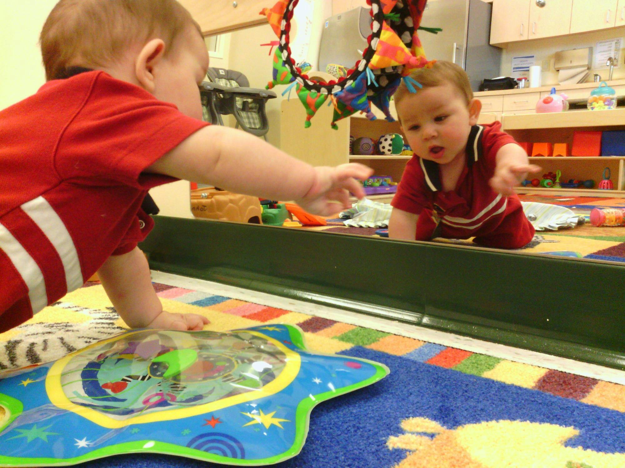 Child reaching for reflection in mirror in a play area