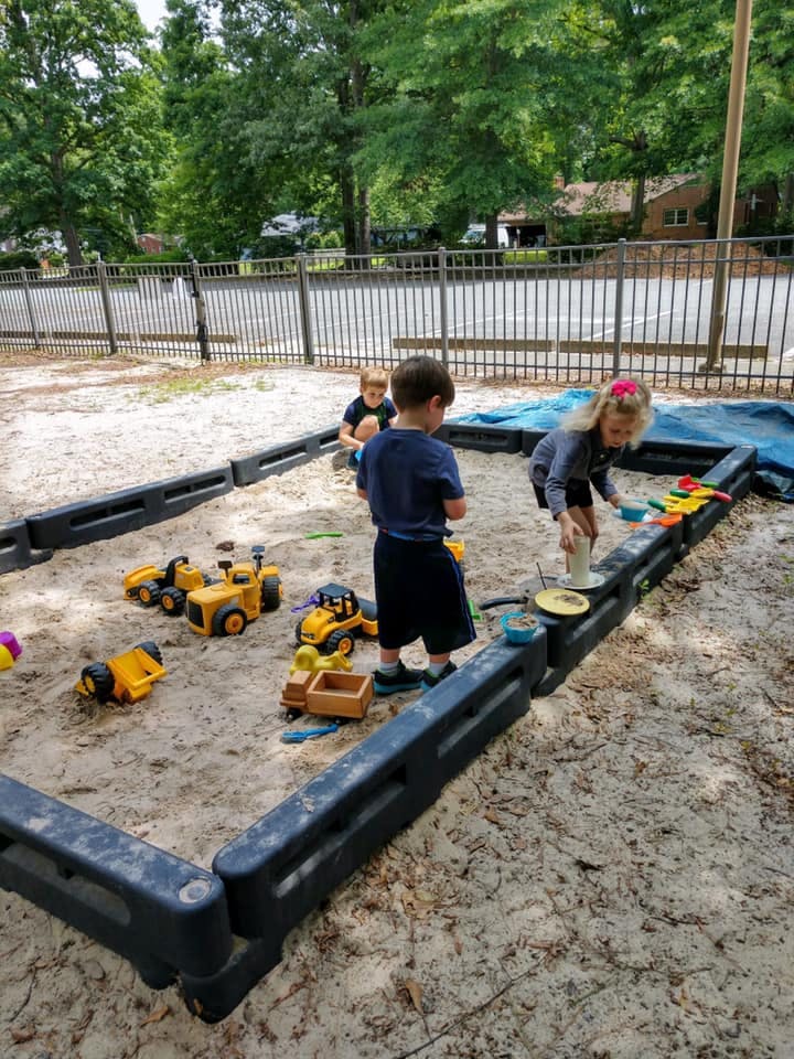 Children playing in a sandbox with toy trucks and sand toys