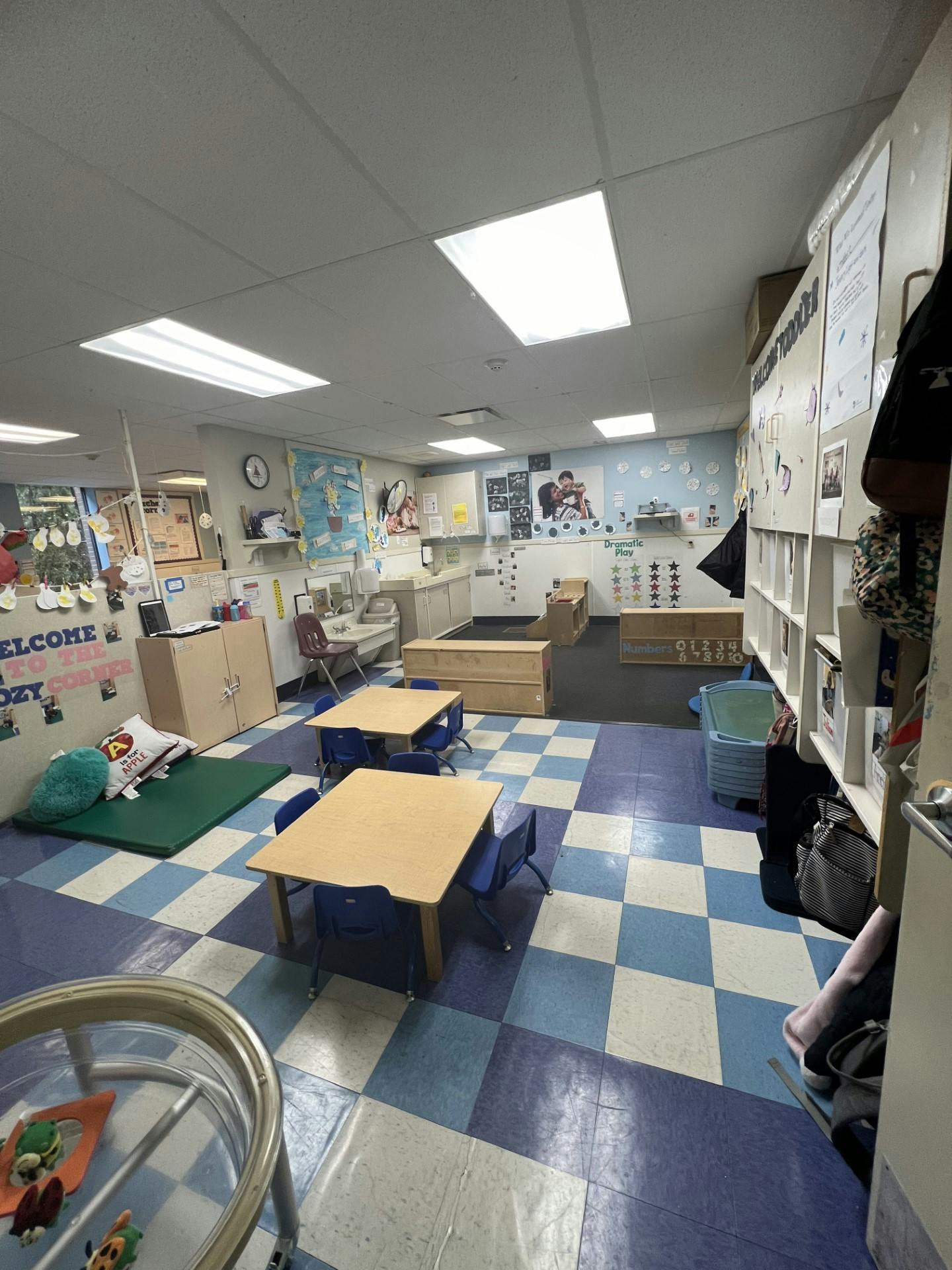 An empty early childhood classroom with small tables, chairs, and play areas