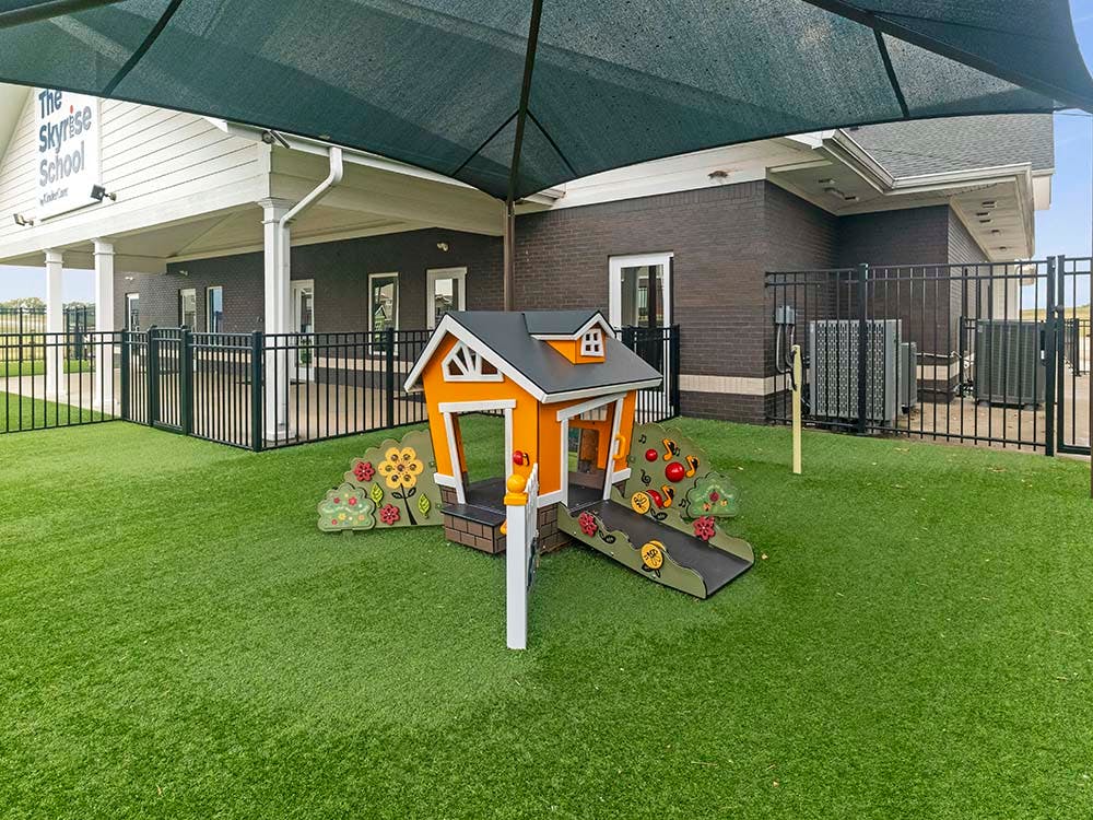 Playground with an orange playhouse, artificial turf, and a building in the background