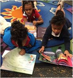 Three children reading books on a colorful rug