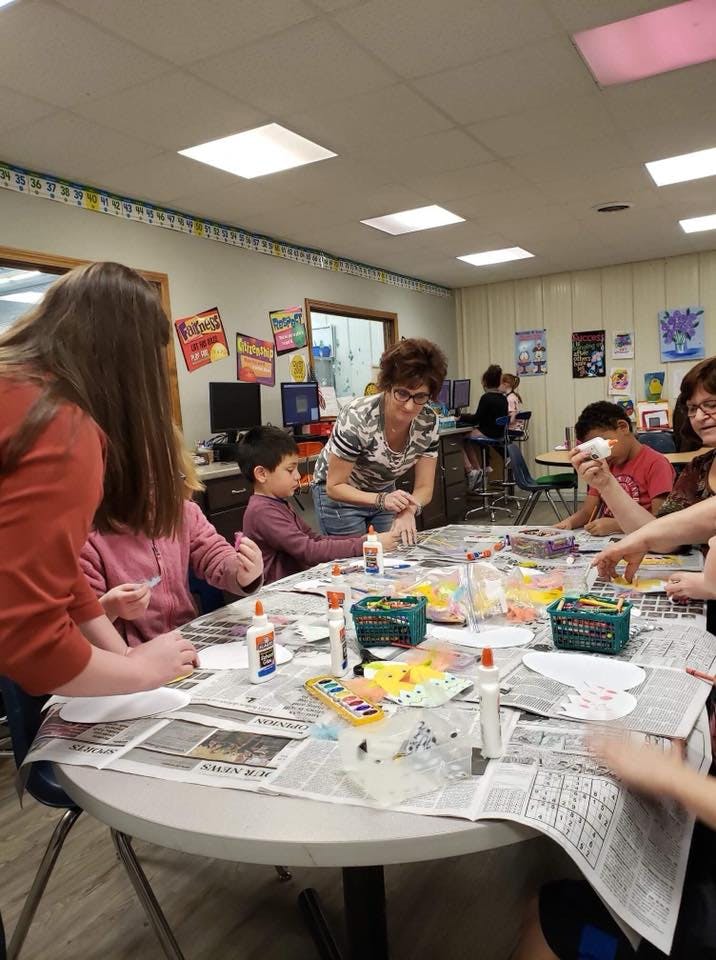 Adults and children doing crafts at a table in a classroom