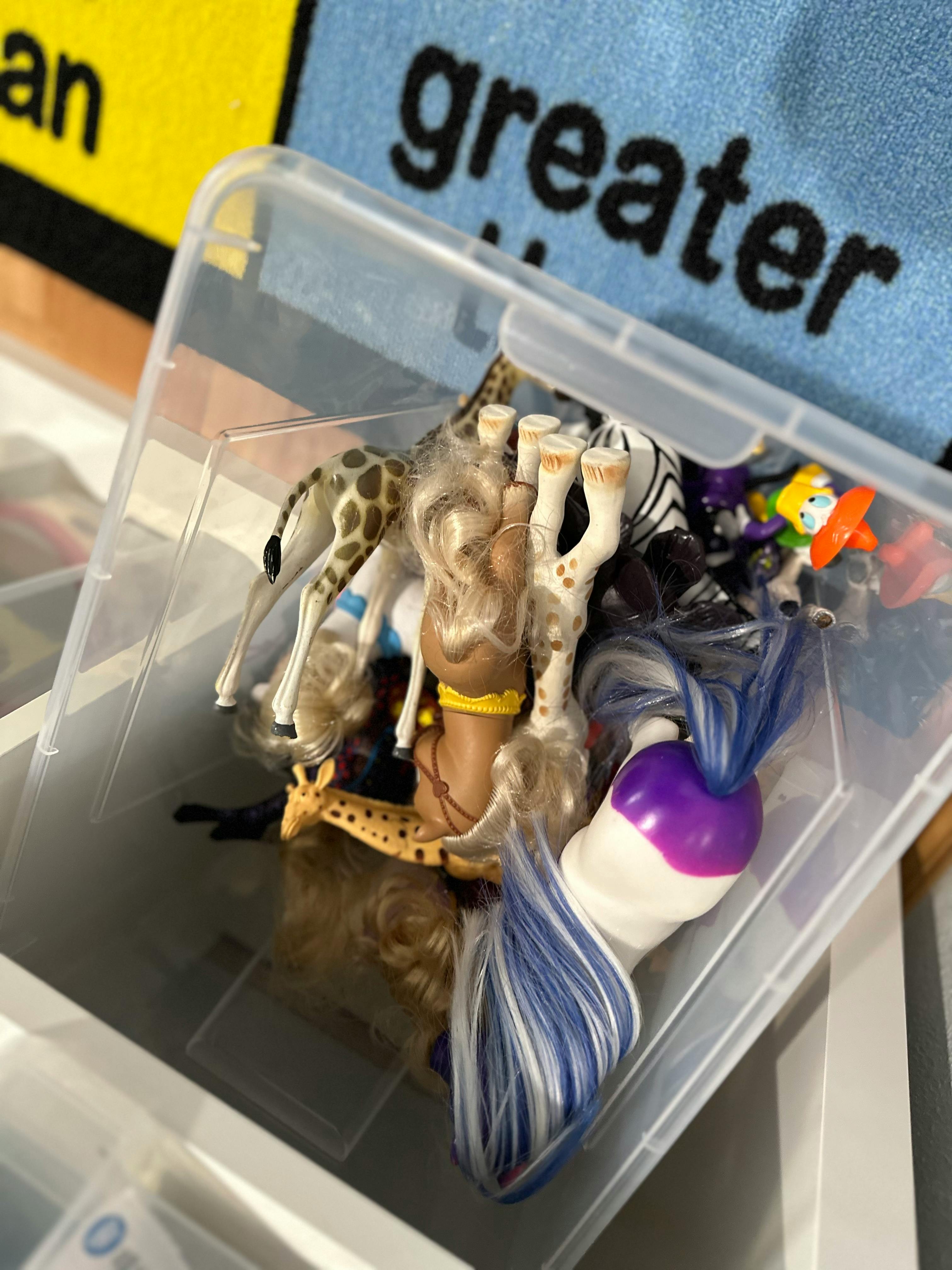 Plastic bin filled with various toys including animal figures and dolls
