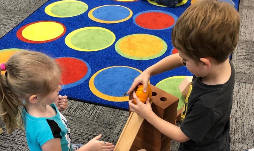 Two children playing with a ball and a wooden ramp toy