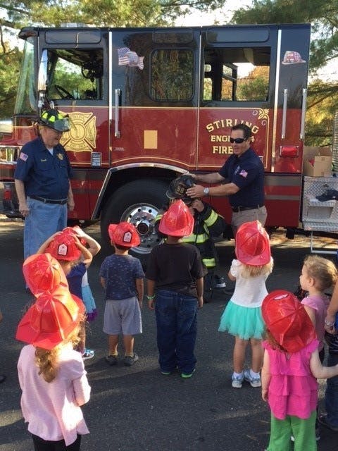 Adults and children in front of a fire truck, one adult helping a child