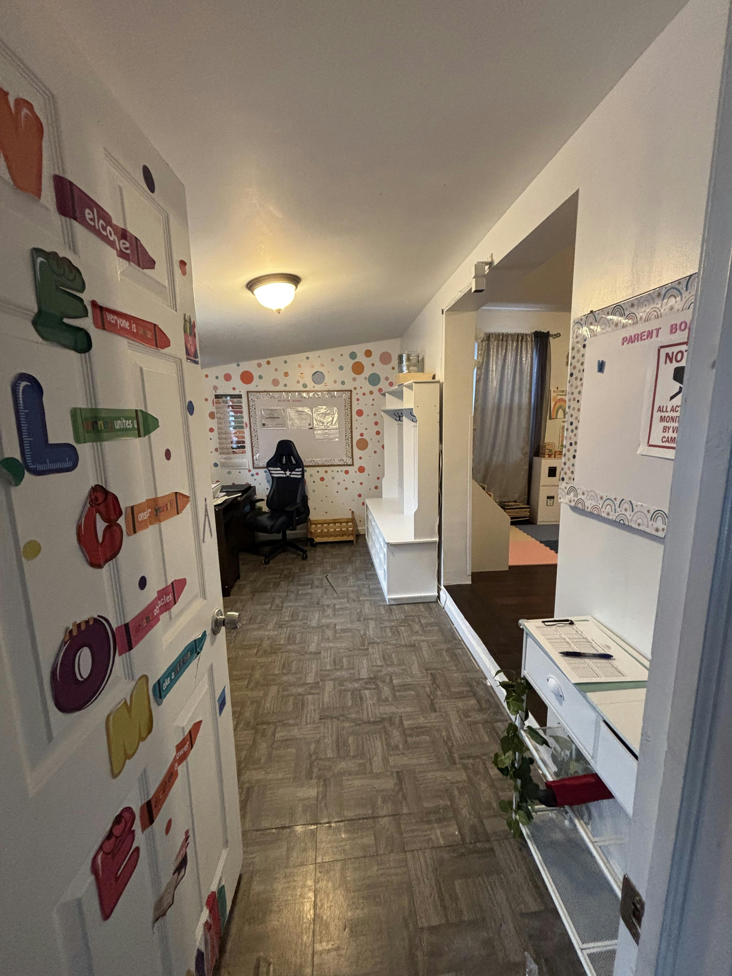 Room with a bulletin board, chair, shelves, and a door decorated with colorful letters and crayons