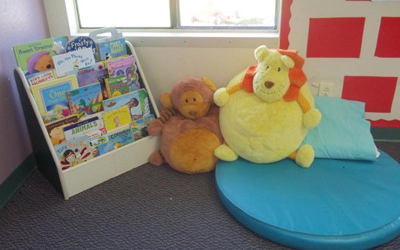 Children's books on a bookshelf with a stuffed lion and monkey toy