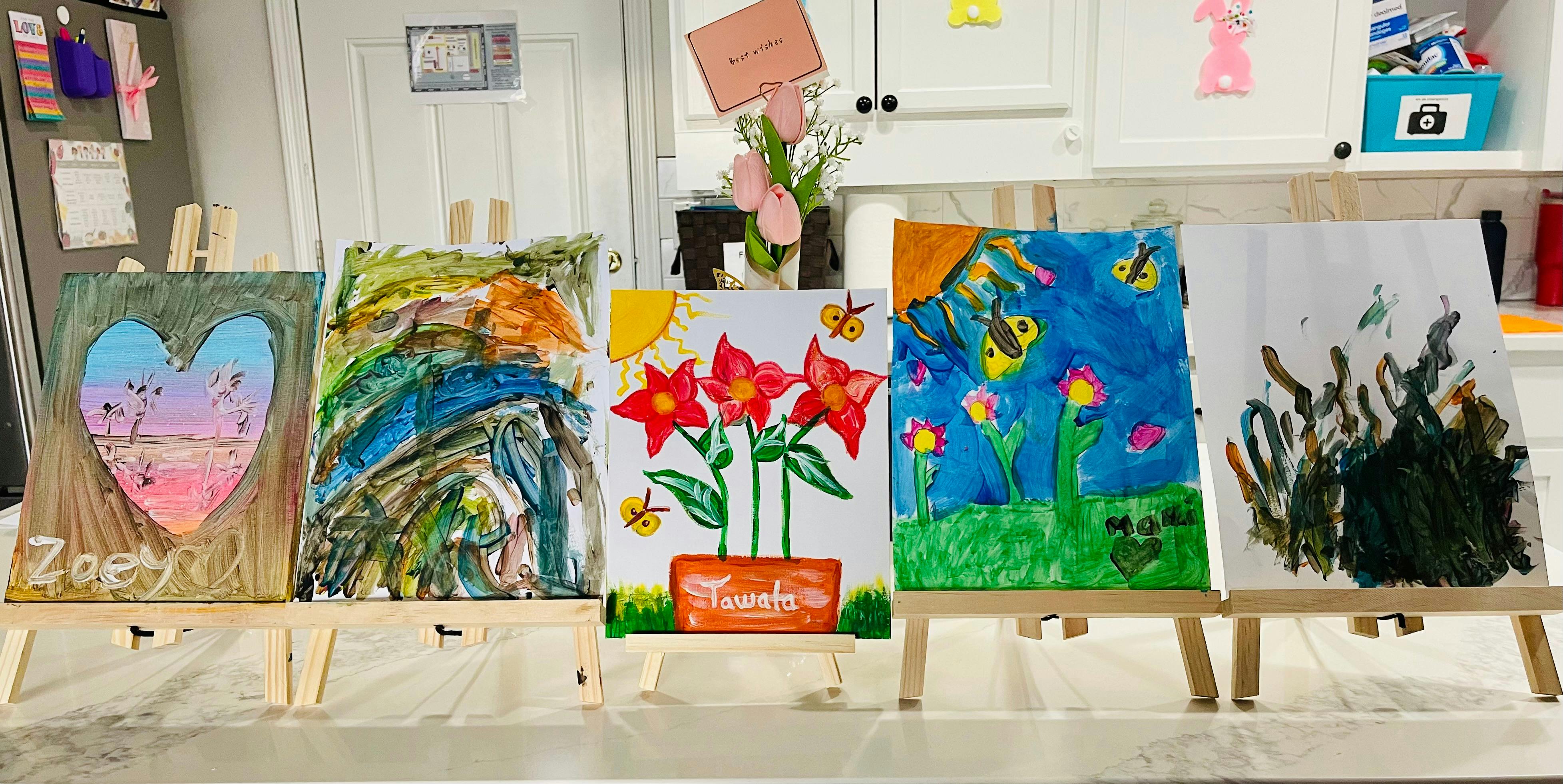 Five children's paintings displayed on small wooden easels