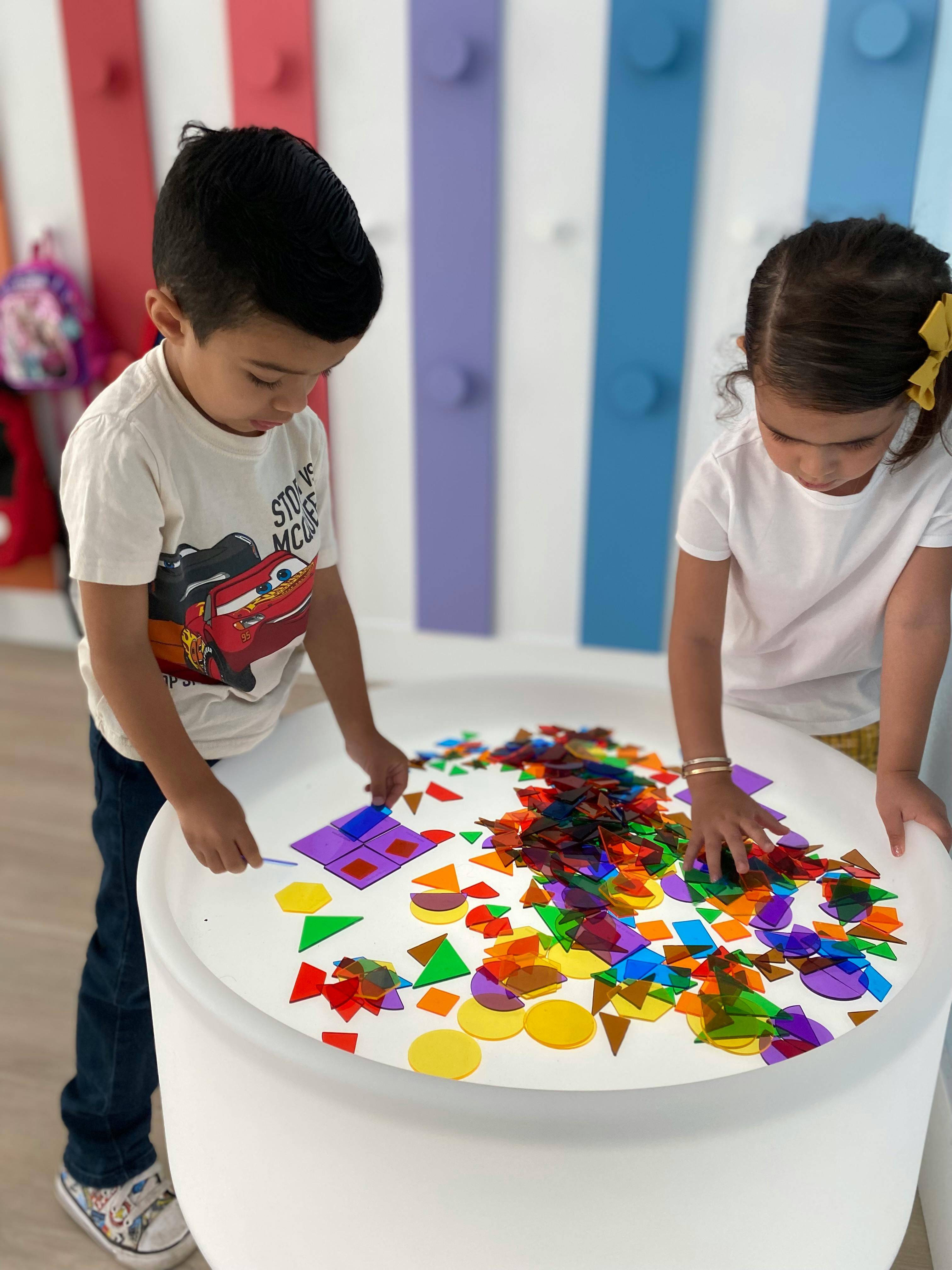 Two children playing with colorful translucent shapes on a light table