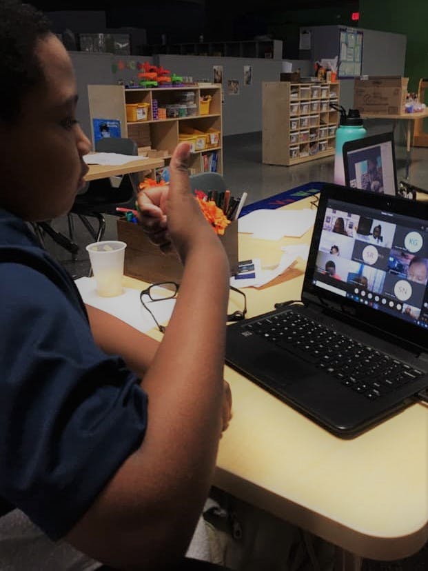 Person giving a thumbs up while looking at a laptop with a video call