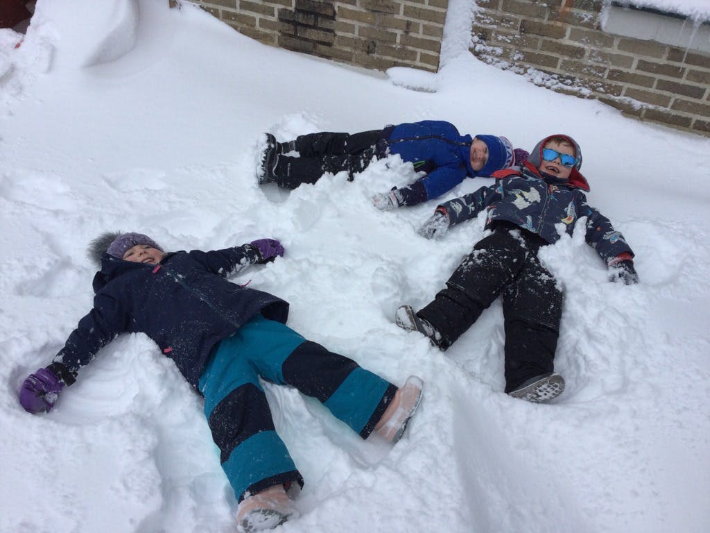 Three children lying in the snow making snow angels