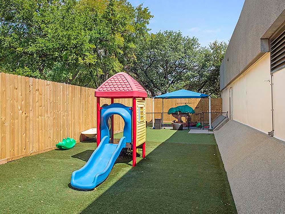 Playground with a small slide, swing, and covered sandbox on a grassy area