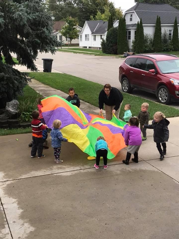 Person and children playing with a colorful parachute