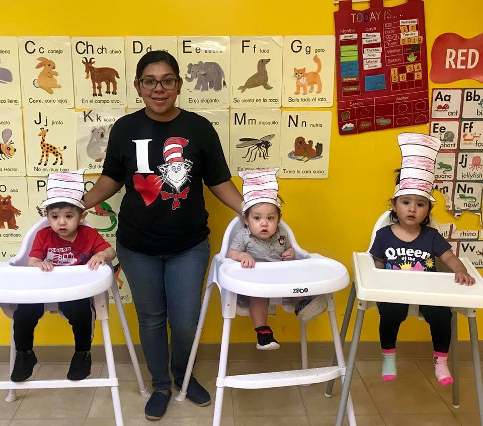 Person standing with three children in high chairs wearing striped hats