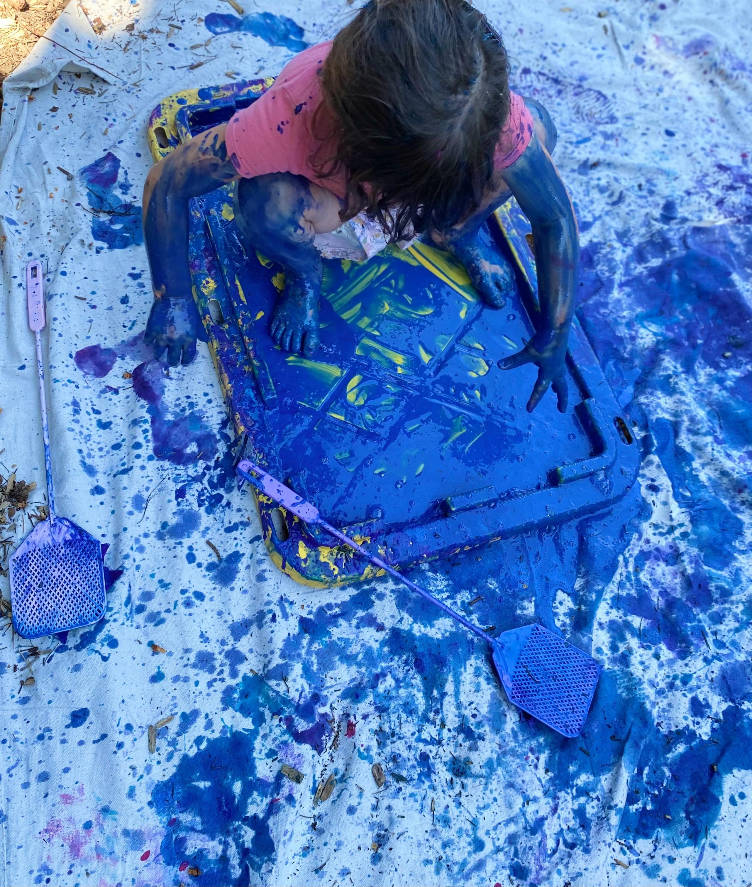 Child covered in blue paint on a tarp