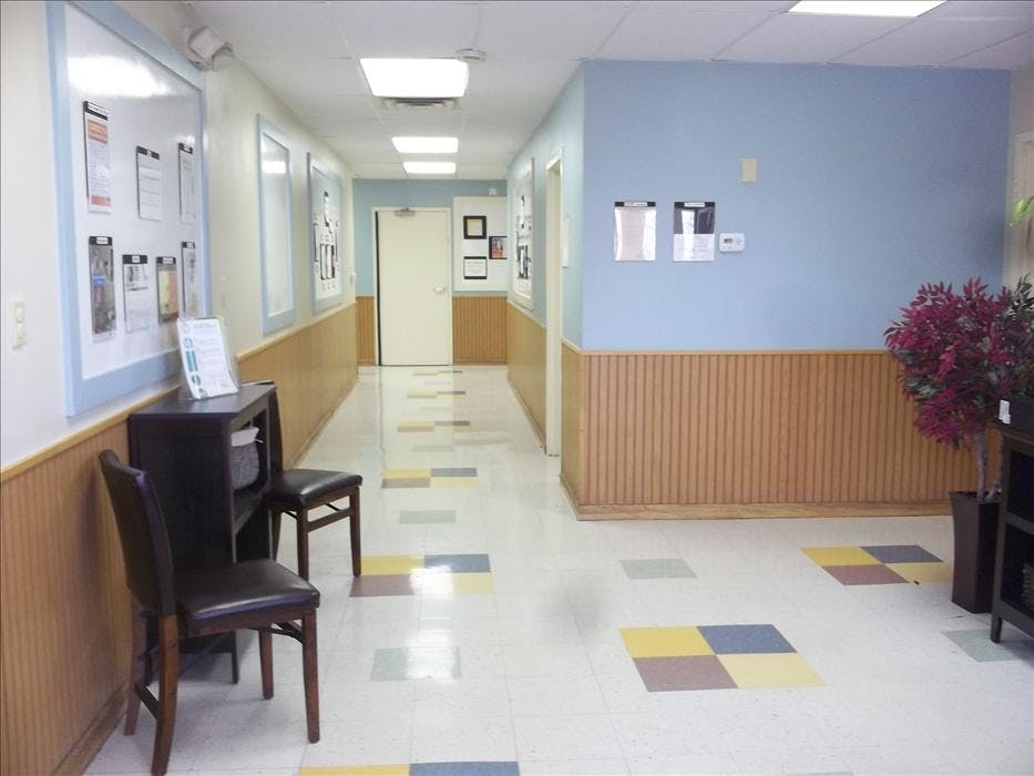 A long, bright hallway with light blue walls, wood wainscoting, and patterned floor tiles