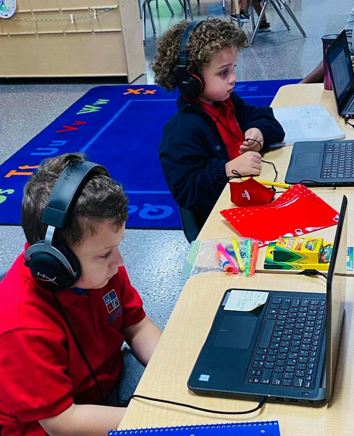 Two children wearing headphones and looking at laptops in a classroom
