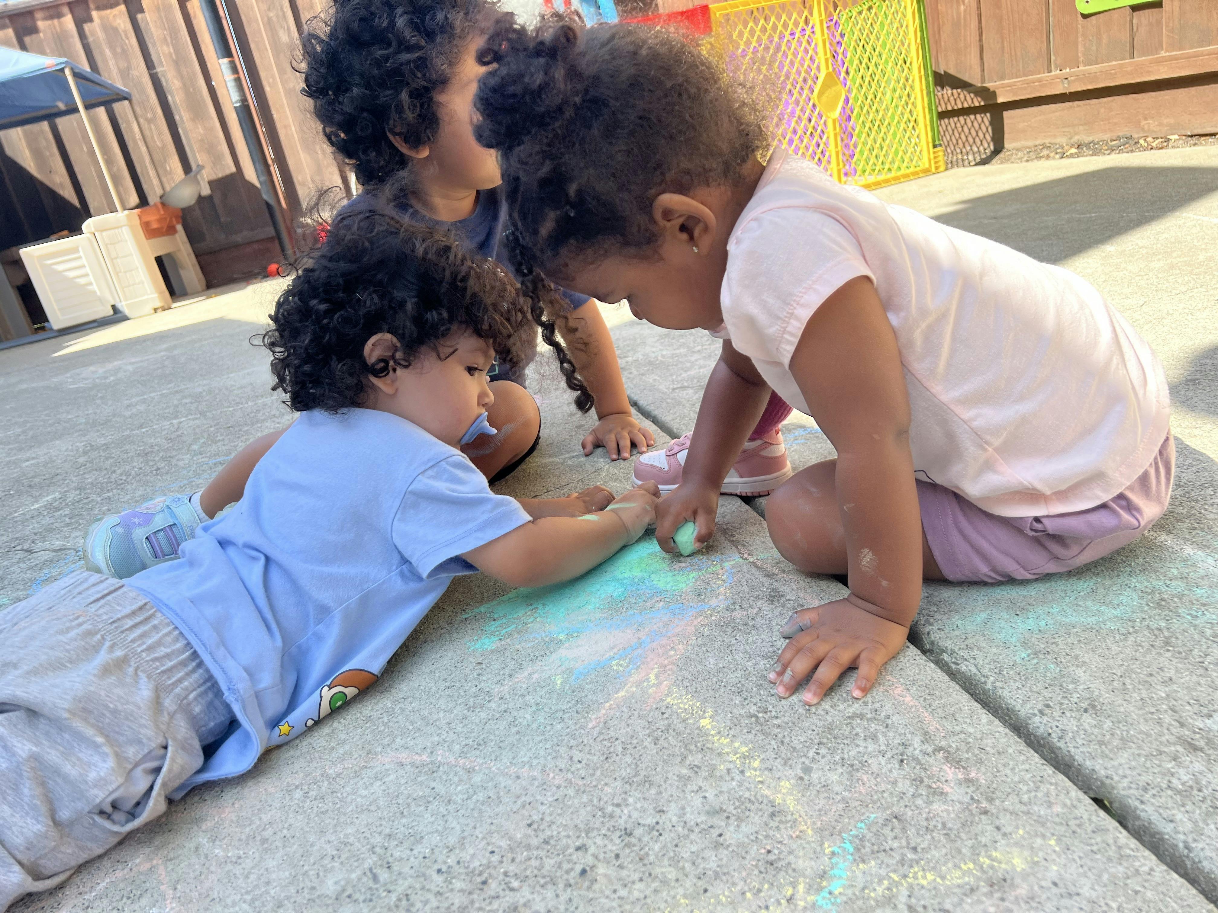 Three children drawing with chalk on pavement