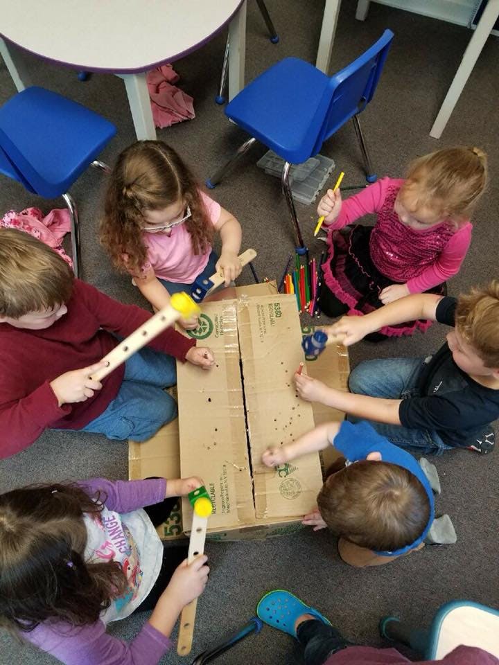 Children playing with a cardboard box and mallets