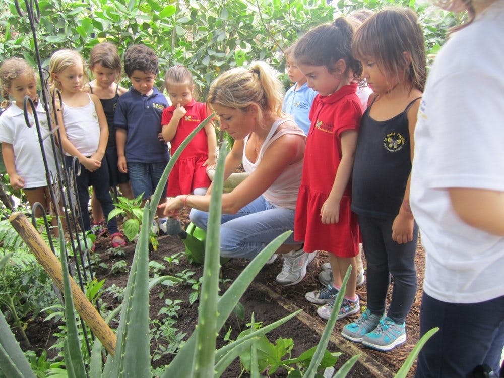 Person crouching in garden with children watching