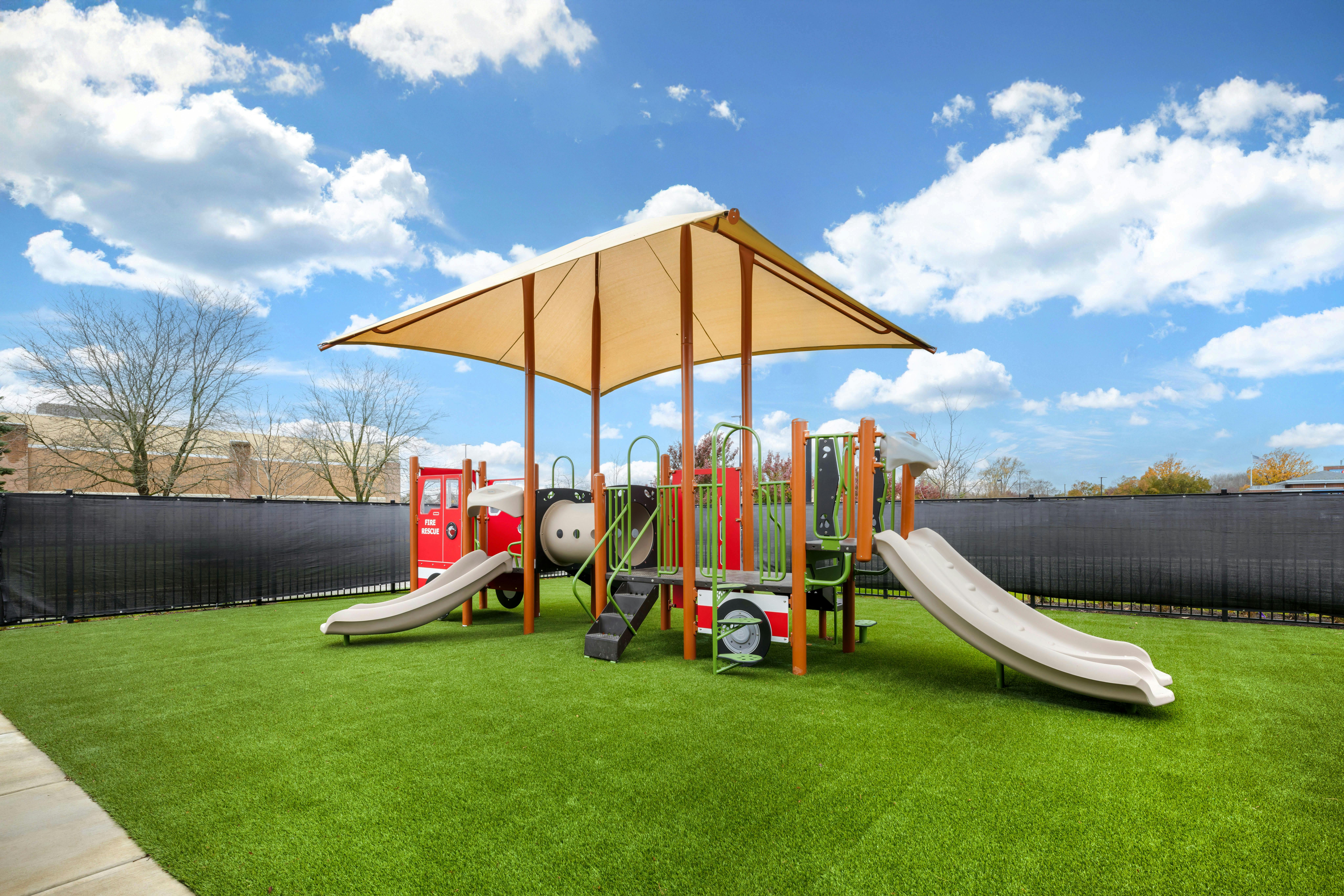 A playground with a fire truck shaped structure and multiple slides under a shade canopy