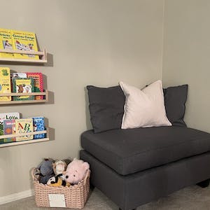 Books on wall shelves next to a dark gray chair and a basket of stuffed animals